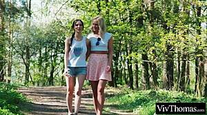 Blonde and brunette ignite with steamy kisses in forest intimacy.