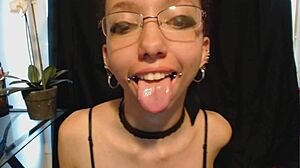 The young goth girl puts on nude lipstick and drools all over it, her tongue and saliva making a mess.